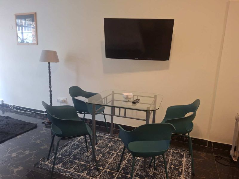 A living area featuring dark tiled flooring and a wall-mounted television, providing a functional space for relaxation and entertainment.