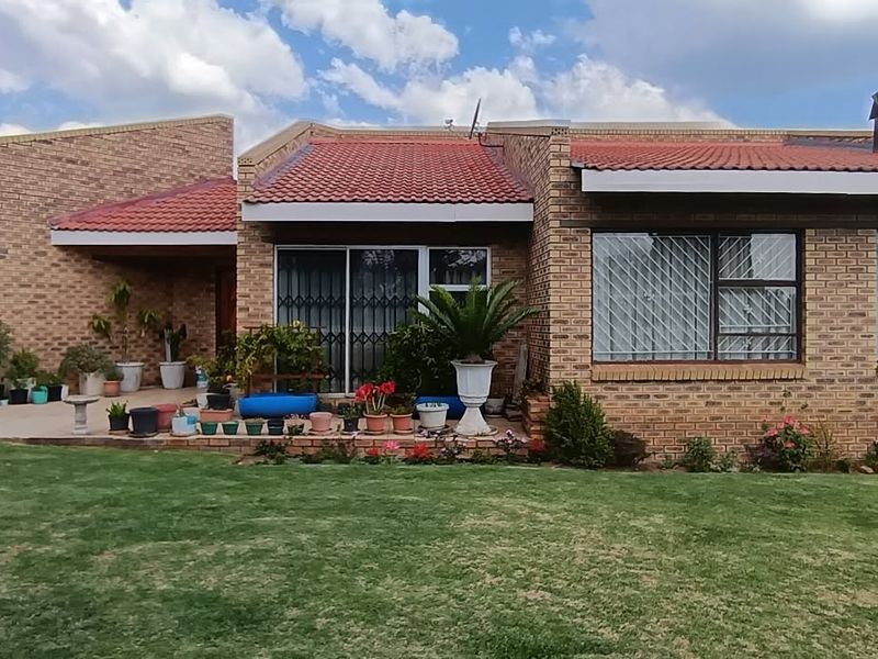 Rear view of a face brick house featuring a tiled roof, paved patio area, and large sliding glass doors with security gates.