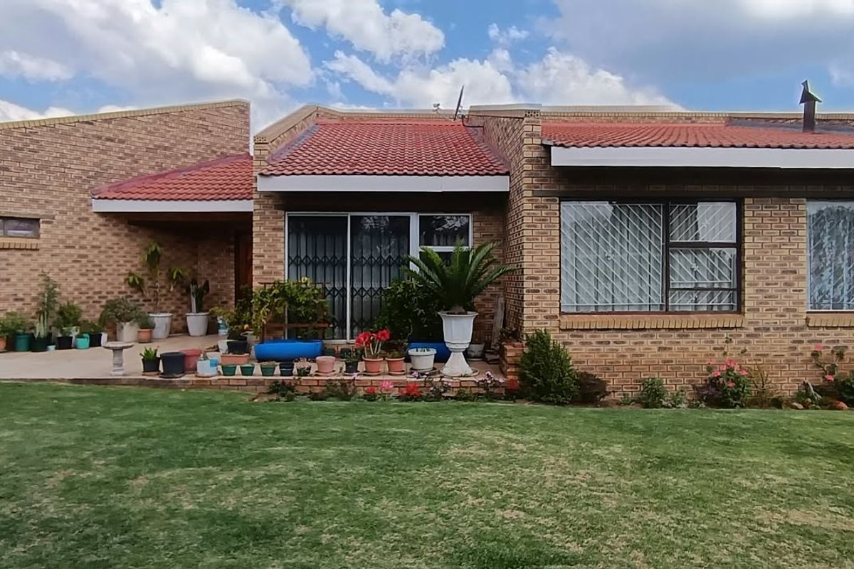 Rear view of a face brick house featuring a tiled roof, paved patio area, and large sliding glass doors with security gates.