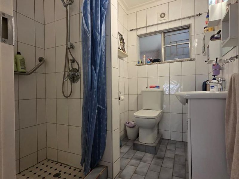 A functional bathroom featuring a walk-in shower with tiled surround, a standard toilet, and a vanity basin with storage.