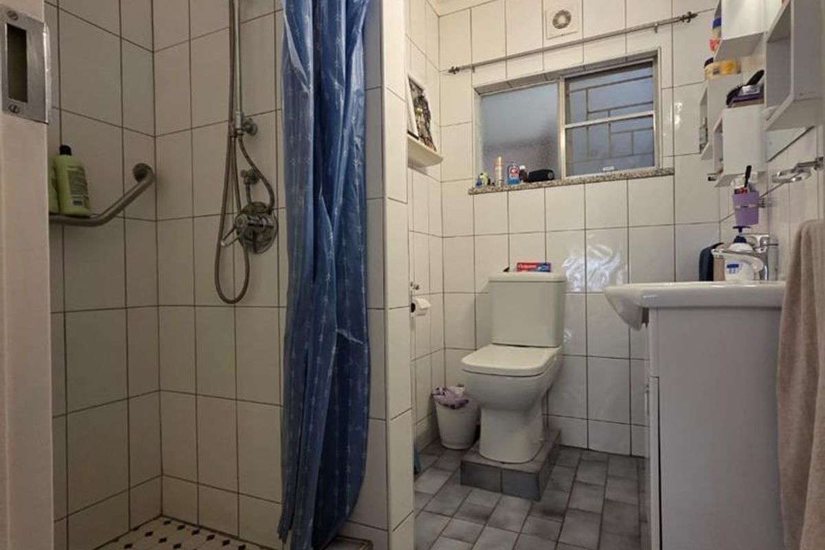A functional bathroom featuring a walk-in shower with tiled surround, a standard toilet, and a vanity basin with storage.
