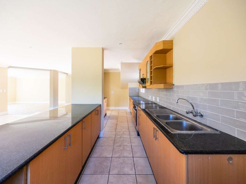 Spacious kitchen featuring granite countertops, double stainless steel sink, subway tile backsplash, and ample wooden cabinetry, flowing into an open-plan living area.