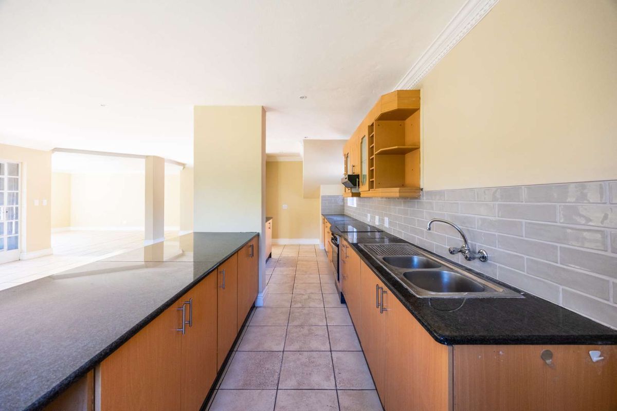 Spacious kitchen featuring granite countertops, double stainless steel sink, subway tile backsplash, and ample wooden cabinetry, flowing into an open-plan living area.