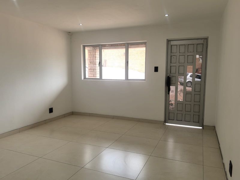 A bright, empty living area featuring neutral tiled flooring, recessed downlights, and a secure aluminium entrance door, offering a clean canvas for interior design.