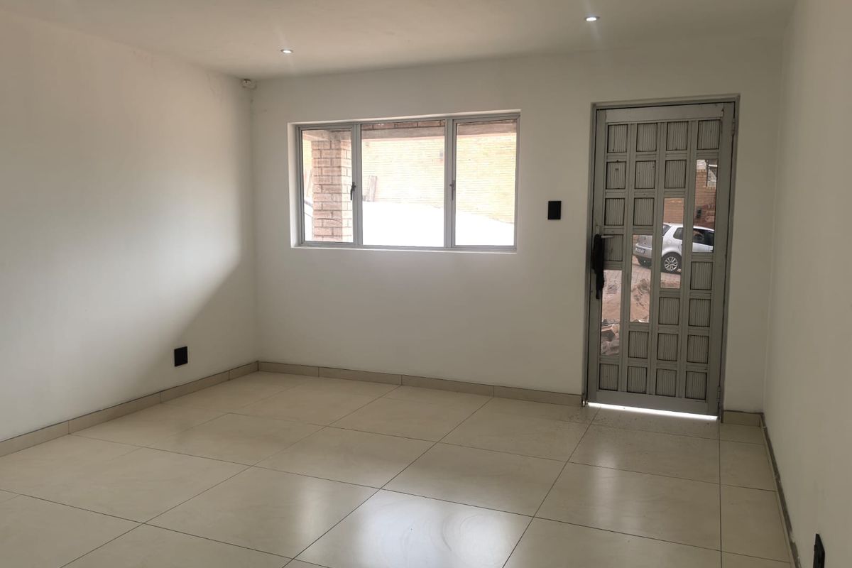 A bright, empty living area featuring neutral tiled flooring, recessed downlights, and a secure aluminium entrance door, offering a clean canvas for interior design.