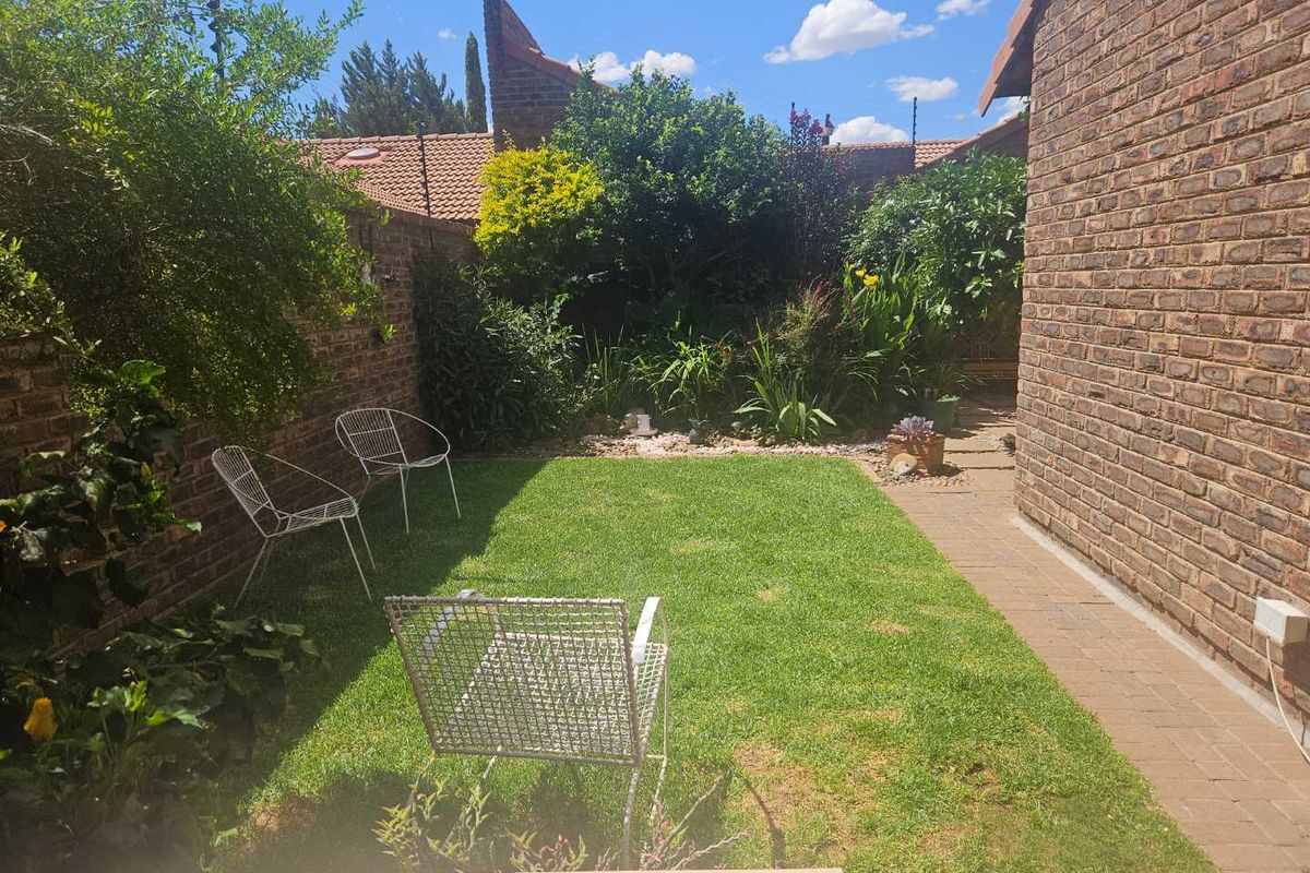 A private rear garden featuring a well-maintained lawn, brick boundary walls, and paved pathways, offering a peaceful outdoor space.