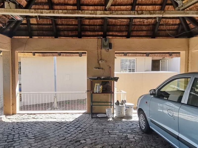 A covered garage area featuring a traditional thatch roof, exposed timber beams, and durable cobblestone paving, providing sheltered parking space.