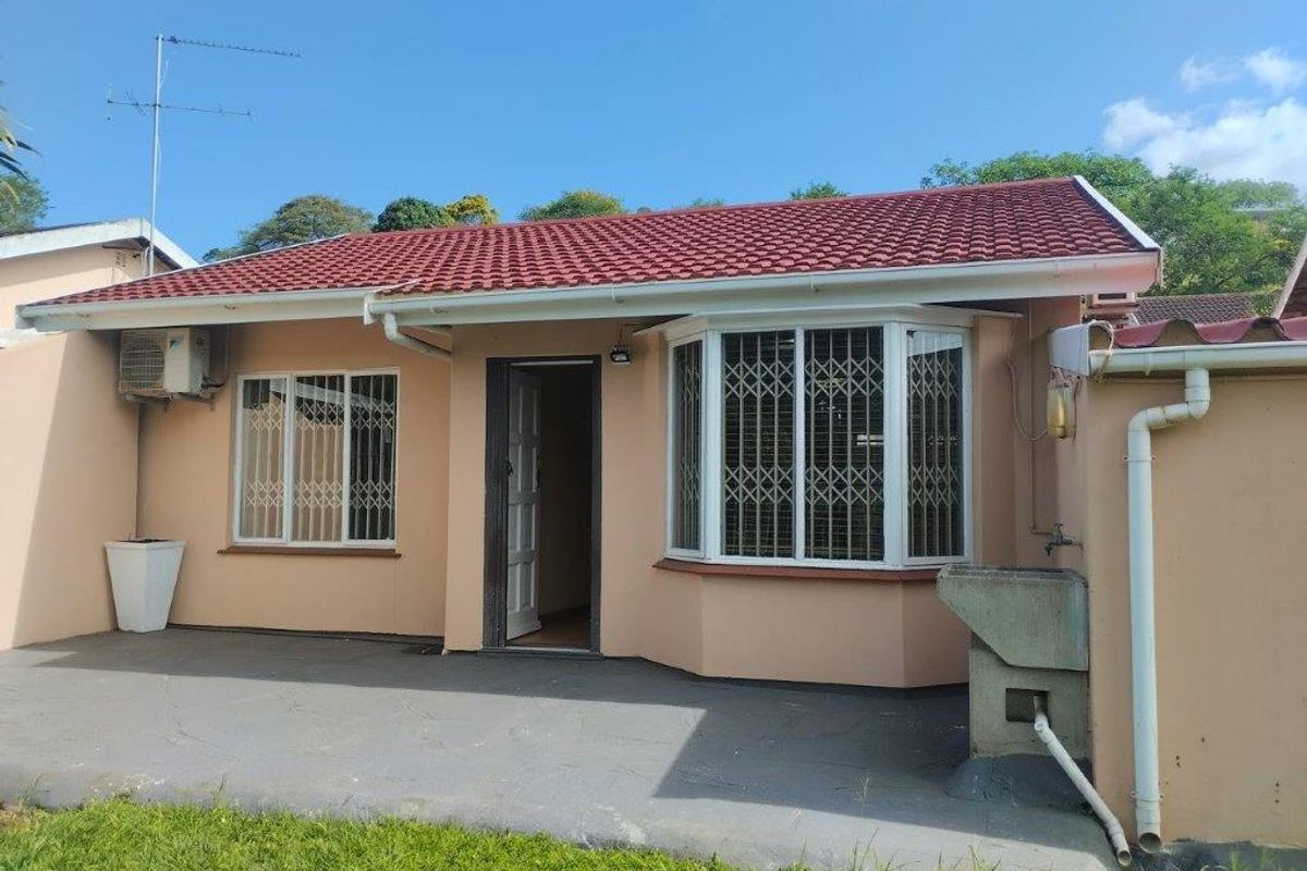 Rear exterior view of the townhouse featuring a tiled roof, bay window with security bars, paved patio area, and an external wash basin.