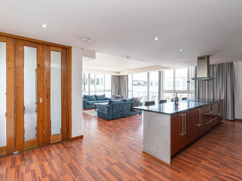 Spacious open-plan living area featuring a modern kitchen island, sleek cabinetry, warm wooden flooring, and large windows providing ample natural light.