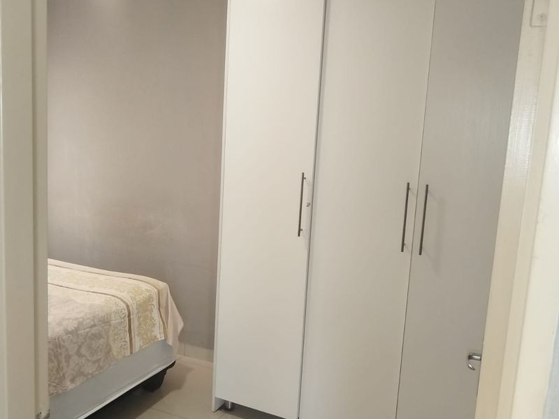 A bedroom featuring tiled flooring and a modern white built-in wardrobe with sleek handles.
