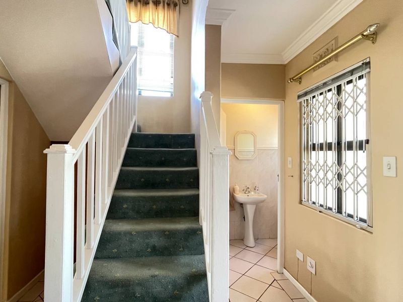 Entrance hall featuring a staircase with carpeted steps, tiled flooring, and access to a guest cloakroom with a pedestal basin.