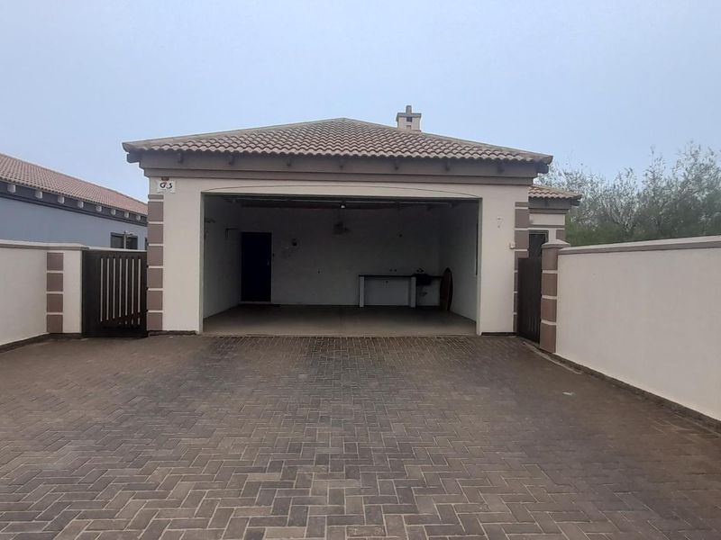 A spacious open-fronted garage with a paved driveway and secure boundary walls, providing ample parking space.