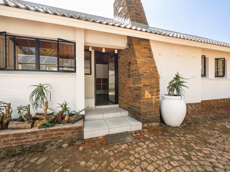 Front entrance of a house featuring a distinctive stone chimney, white painted brick facade, tiled roof, and a brick-paved driveway.