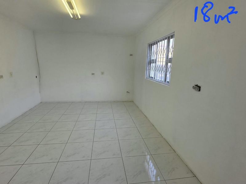 An empty 18 square meter office space featuring tiled flooring, security bars on windows, and standard electrical points.