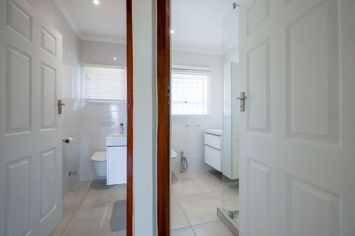 A modern, well-maintained bathroom featuring a wall-hung vanity, concealed cistern toilet, and a glass-enclosed shower area with neutral floor tiling.