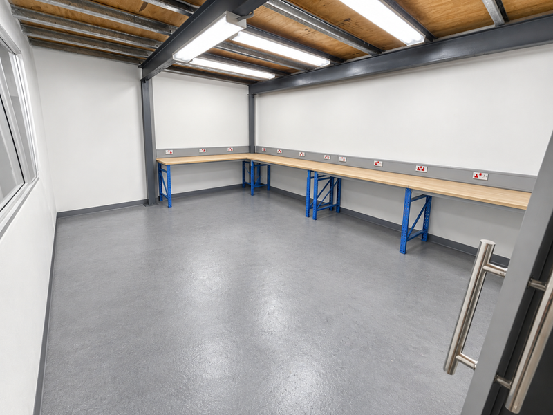 A clean, modern utility or workshop space featuring exposed steel ceiling beams, durable epoxy flooring, and a long built-in workbench with integrated power outlets.