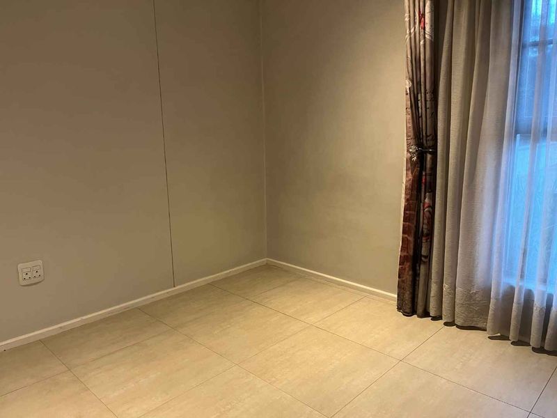An empty bedroom featuring neutral wall paint, tiled flooring, and a window with installed curtain tracks.