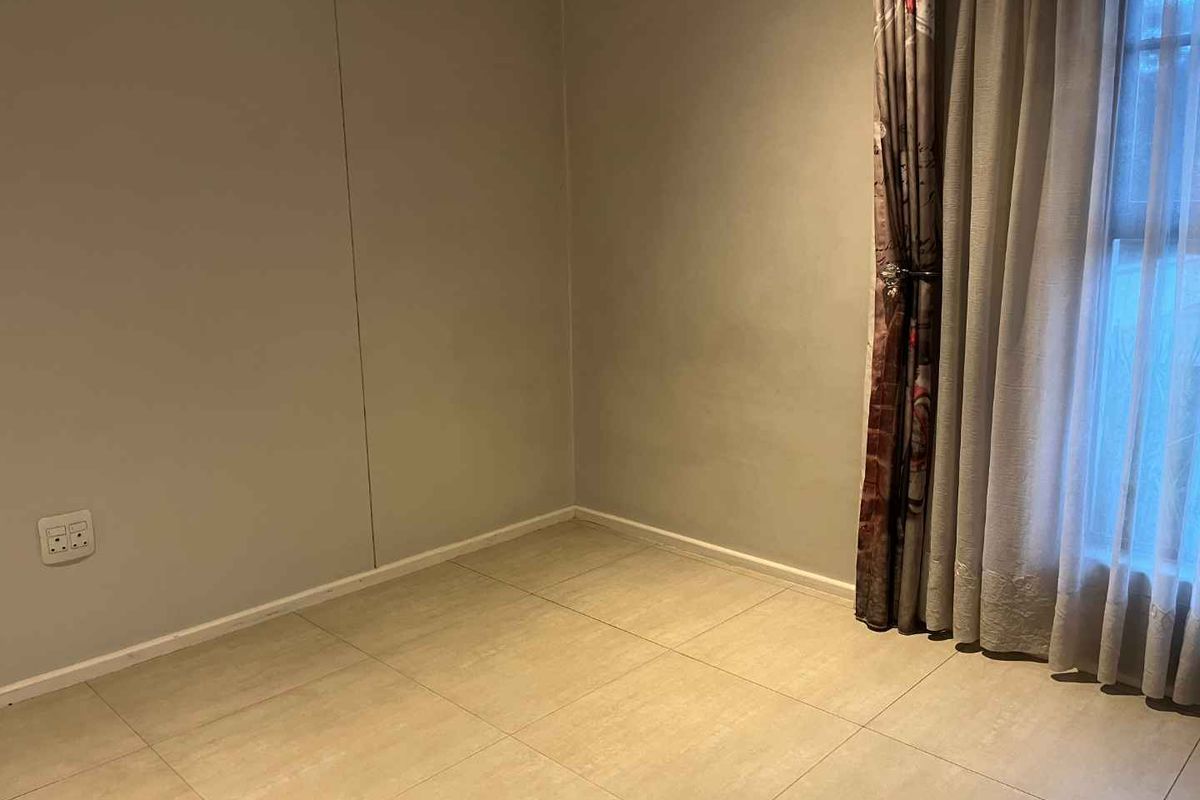 An empty bedroom featuring neutral wall paint, tiled flooring, and a window with installed curtain tracks.