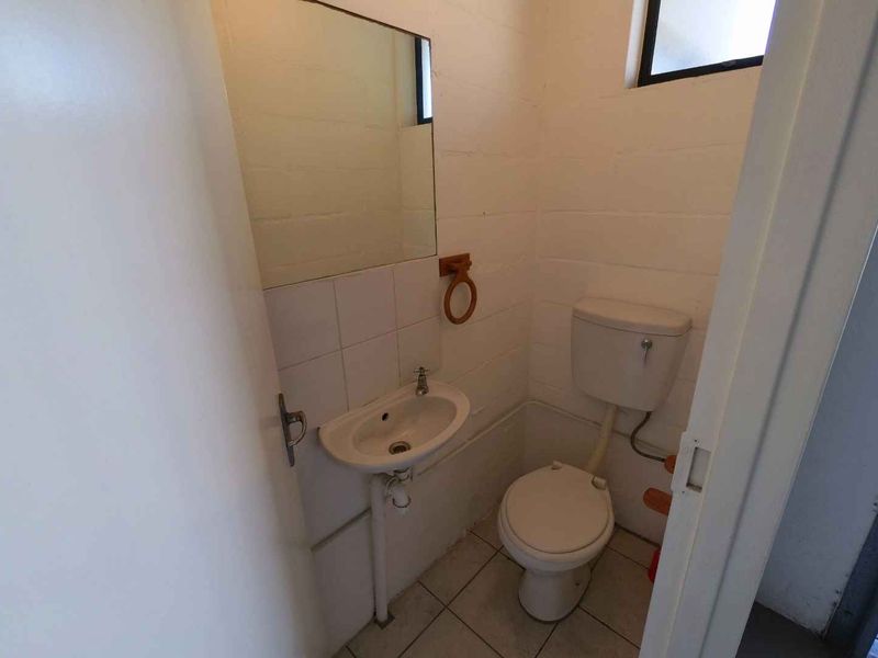 A compact industrial-style bathroom featuring a standard toilet, wall-mounted basin, and mirror with tiled flooring and splashback.