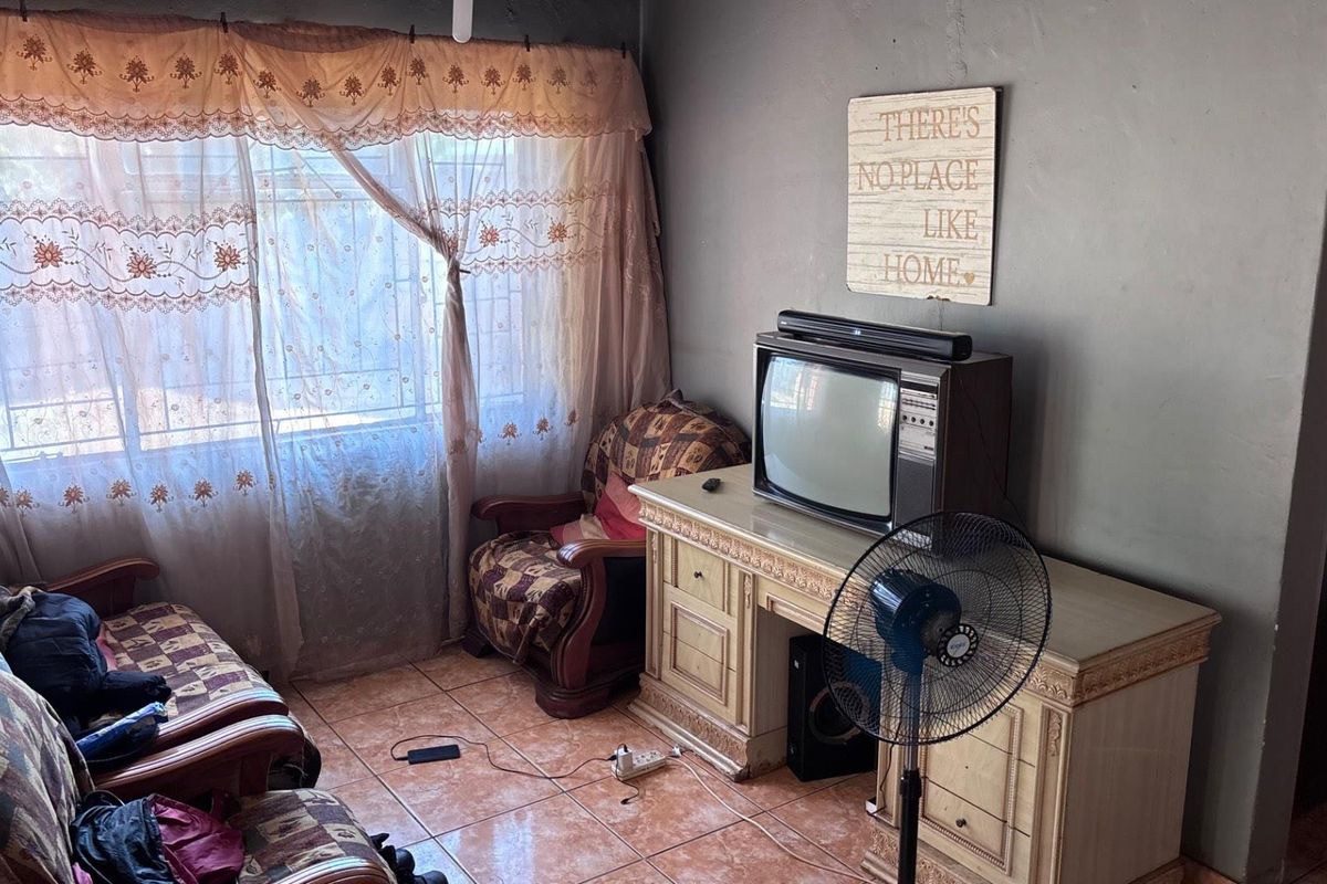 A living room featuring tiled flooring and a window with security bars, offering a functional space for relaxation.