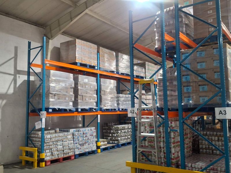 Industrial warehouse space featuring extensive pallet racking systems, exposed steel roof structure, and a functional utility sink area.