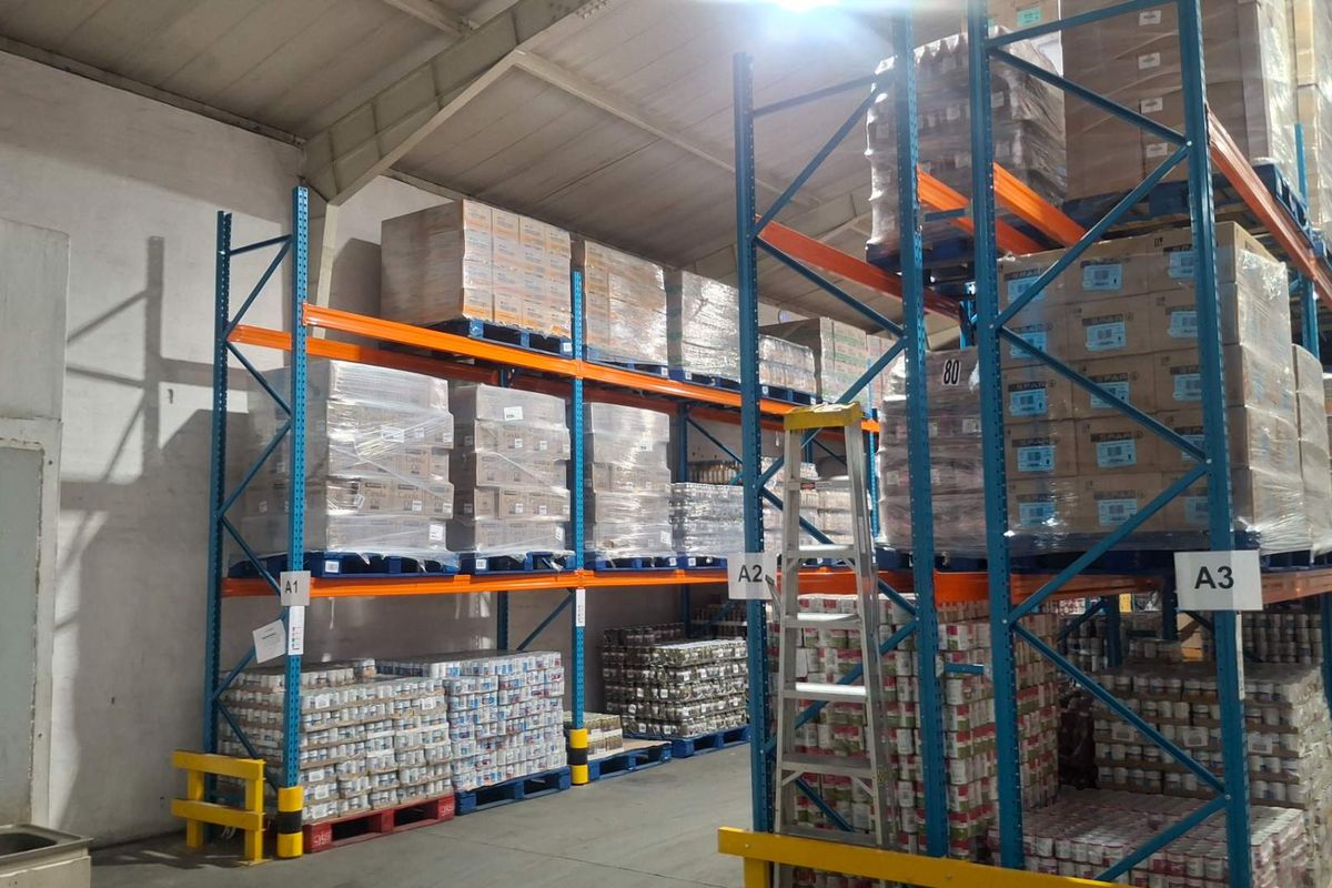 Industrial warehouse space featuring extensive pallet racking systems, exposed steel roof structure, and a functional utility sink area.