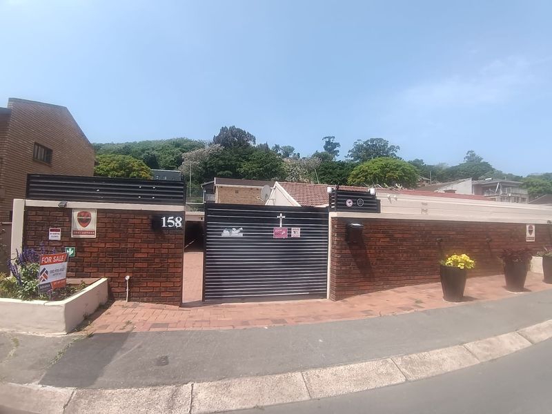 Front exterior view of the property featuring a brick boundary wall, secure metal sliding gate, and paved driveway access from the street.