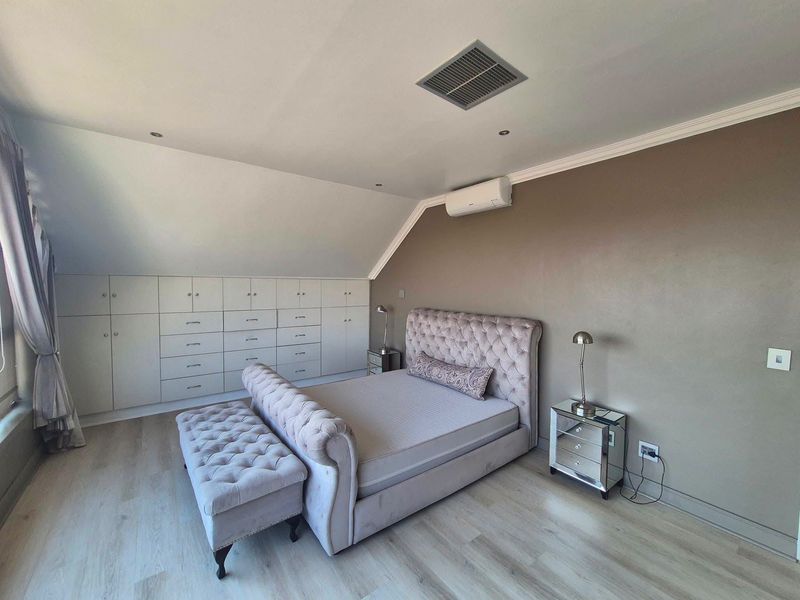 A well-maintained bedroom featuring extensive built-in cabinetry, laminate flooring, recessed lighting, and a wall-mounted air conditioning unit.