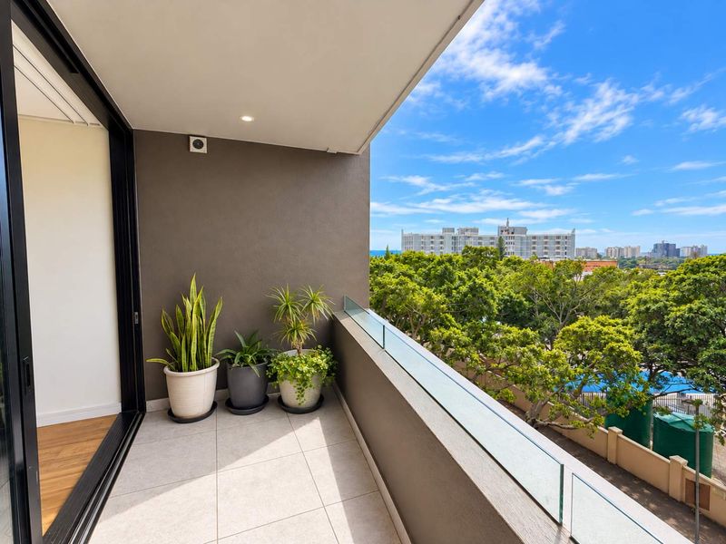 A modern, well-maintained balcony featuring a sleek glass balustrade, tiled flooring, and recessed lighting, offering pleasant elevated views of the surrounding neighborhood.