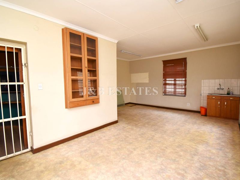 Open plan retail or office space featuring a small kitchenette area, built-in wall cabinetry, and security gate access.