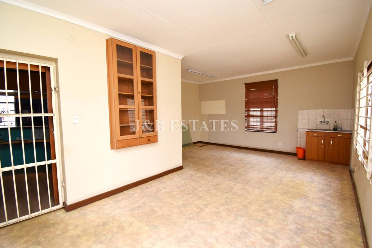 Open plan retail or office space featuring a small kitchenette area, built-in wall cabinetry, and security gate access.