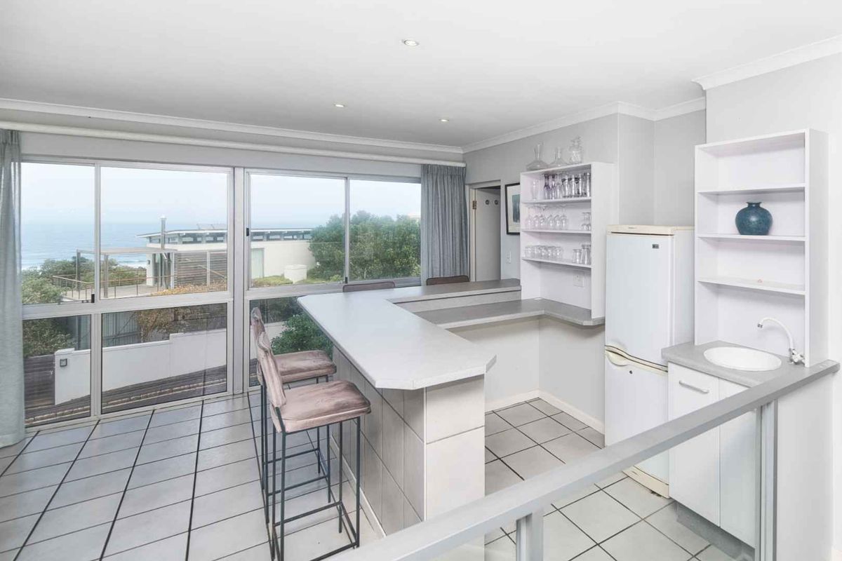 A functional kitchen area featuring a breakfast bar, tiled flooring, and large sliding glass doors offering scenic coastal views.