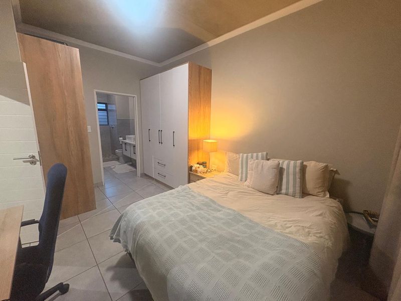 A well-maintained bedroom featuring built-in cupboards, tiled flooring, and direct access to an en-suite bathroom.