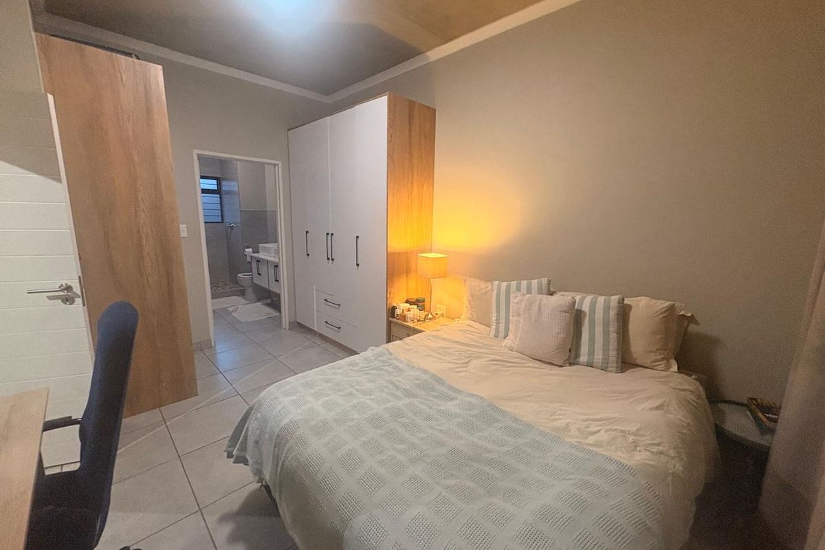 A well-maintained bedroom featuring built-in cupboards, tiled flooring, and direct access to an en-suite bathroom.