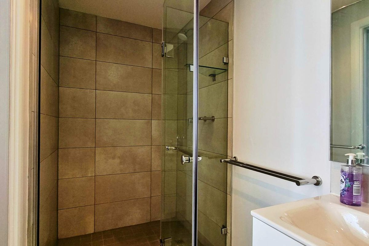 Modern bathroom featuring a glass-enclosed shower with neutral wall tiling, a vanity basin, and a wall-mounted towel rail.