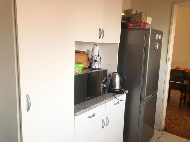 A compact kitchen area featuring white built-in cabinetry, a laminate countertop, and space for a refrigerator.