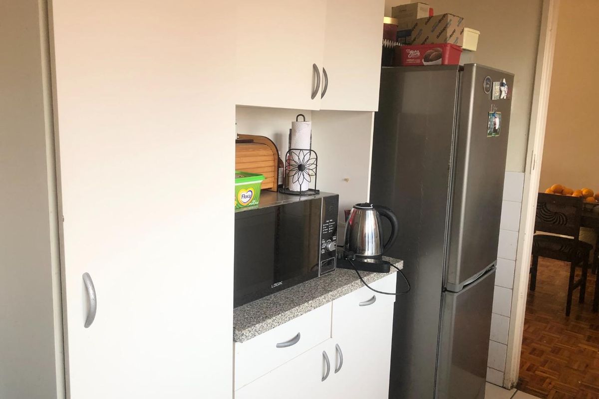 A compact kitchen area featuring white built-in cabinetry, a laminate countertop, and space for a refrigerator.