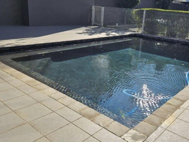 A private swimming pool area featuring a paved deck and safety fencing, providing a functional outdoor space for relaxation.