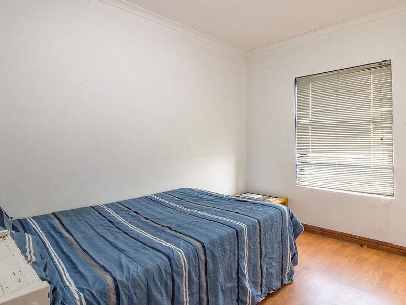 A bedroom featuring laminate flooring, white walls with coving, and venetian blinds. The space requires cosmetic updates to improve its overall condition.