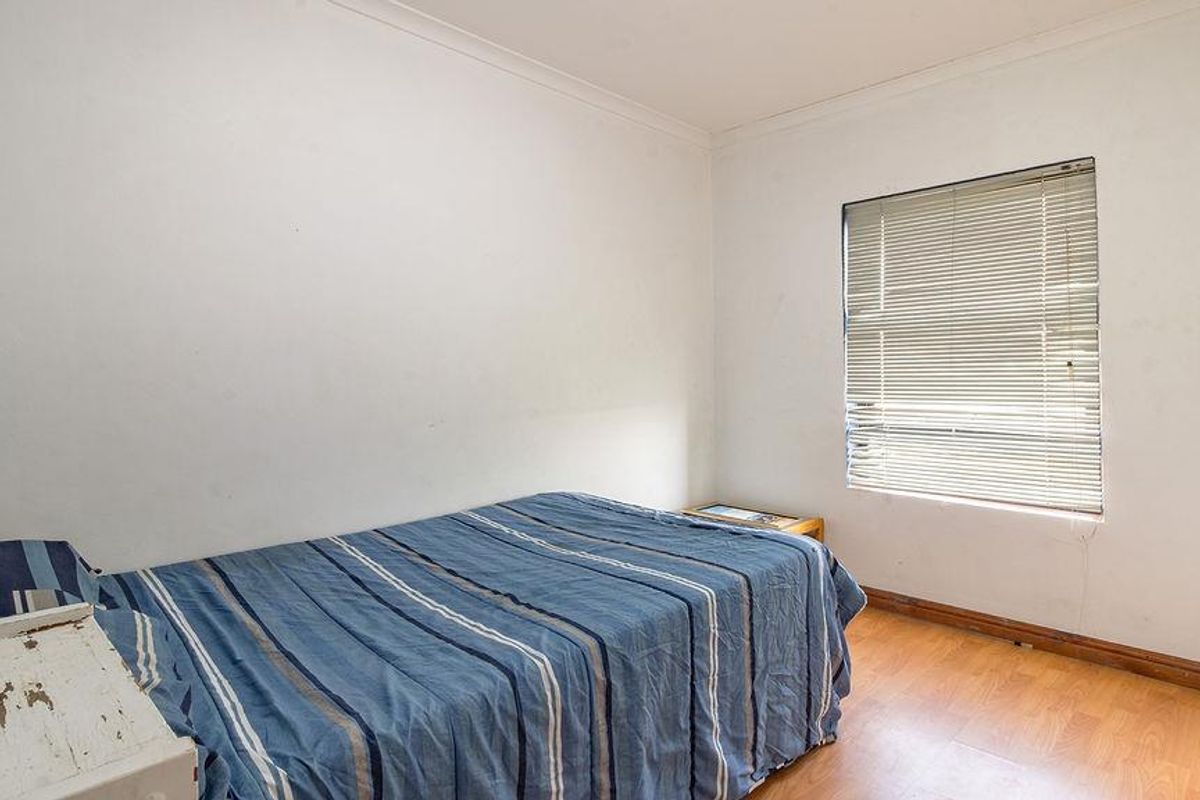 A bedroom featuring laminate flooring, white walls with coving, and venetian blinds. The space requires cosmetic updates to improve its overall condition.