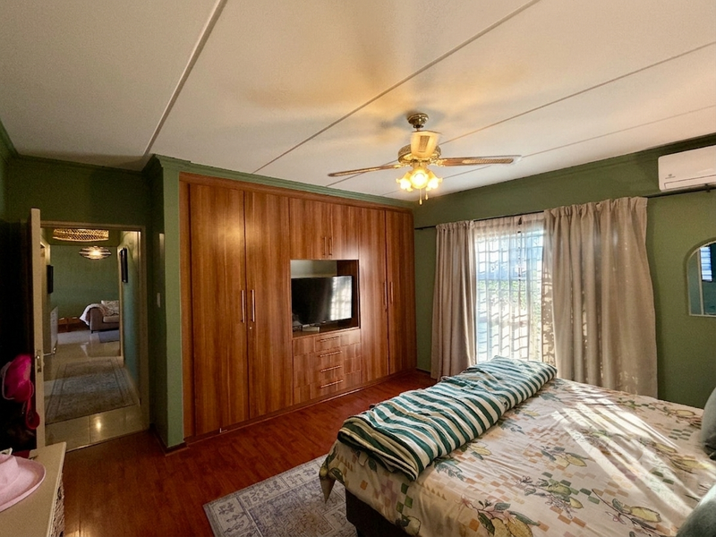 Spacious bedroom featuring extensive built-in wooden cabinetry, laminate flooring, a ceiling fan, and a wall-mounted air conditioning unit.