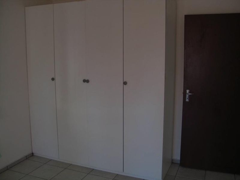 A bedroom featuring a large white built-in wardrobe, tiled flooring, and a dark internal door.
