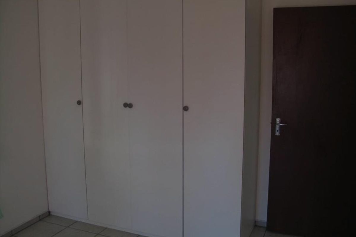 A bedroom featuring a large white built-in wardrobe, tiled flooring, and a dark internal door.