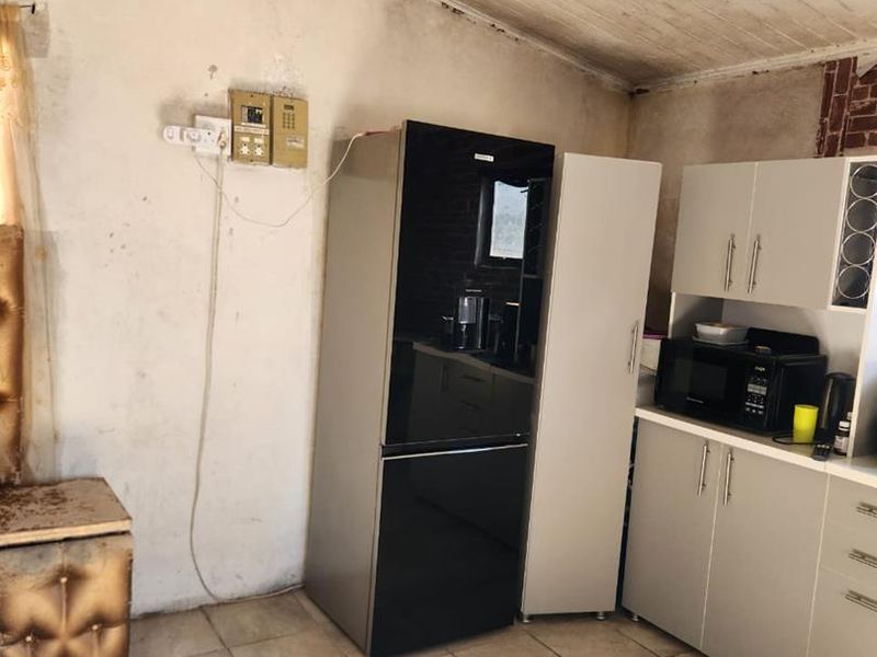 A dated kitchen area featuring tiled floors, built-in cabinetry, and a timber panelled ceiling, currently showing signs of wear and requiring cosmetic updates.
