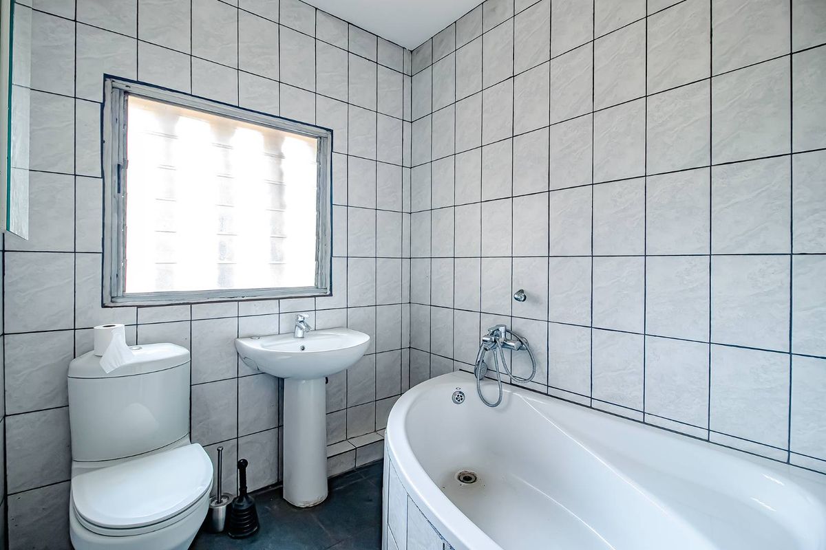 A functional bathroom featuring a pedestal sink, a white toilet, and a bathtub with a handheld shower fixture, finished with full-height wall tiling.