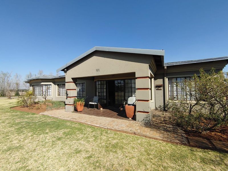 Front elevation of a small holding residence featuring a covered patio, brick paved entrance, and security-barred windows under a metal roof structure.