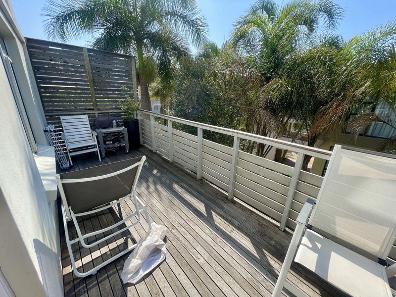 An outdoor balcony featuring timber decking and a privacy screen, offering a private space for relaxation with views of surrounding trees.