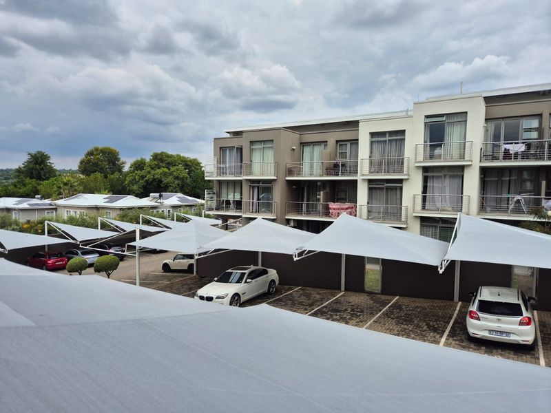 Exterior view of an apartment complex featuring covered parking bays with shade cloth structures and multi-level balconies with metal railings.