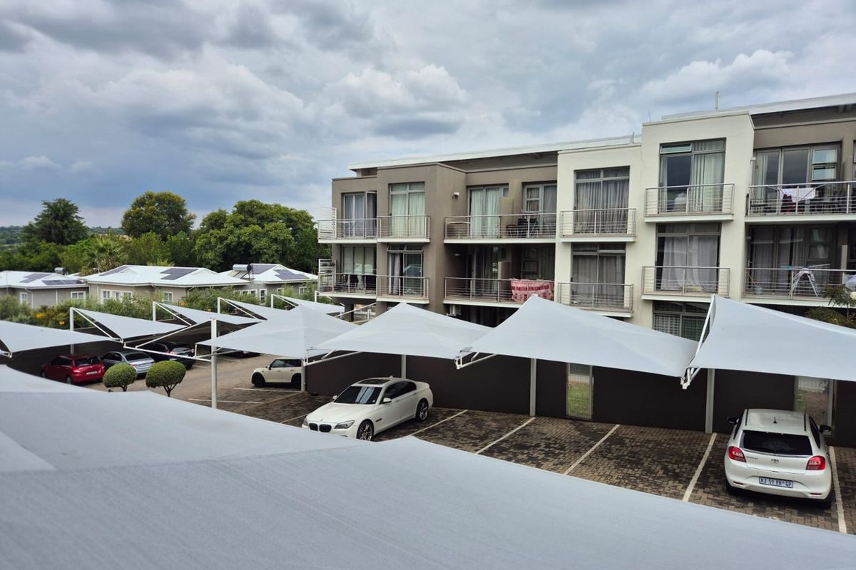 Exterior view of an apartment complex featuring covered parking bays with shade cloth structures and multi-level balconies with metal railings.