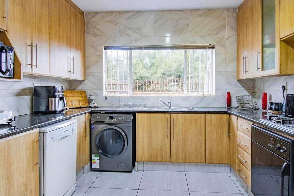 A functional kitchen featuring light wood cabinetry, granite countertops, tiled backsplash, and integrated space for laundry and dishwashing appliances.